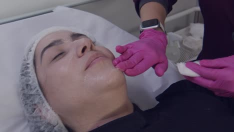 Anonymous-beautician-rubbing-anesthetic-gel-onto-patient's-face-before-cosmetic-surgery
