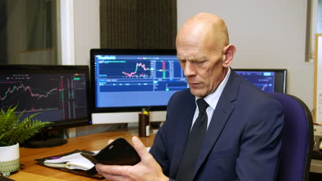 A-mature-business-man-stock-broker-checking-his-phoneand-messaging-in-his-trading-office