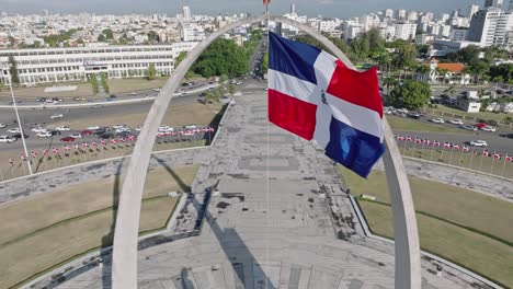 Aerial-view-of-waving-flag-of-Dominican-Republic-at-Plata-de-la-Bandera-and-Cityscape-of-Santo-Domingo-in-background