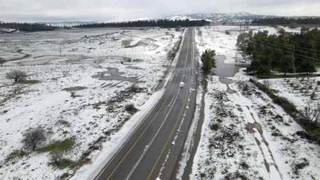 Vehicles-driving-through-snow-covered-countryside-with-mountains-in-background,-Israel