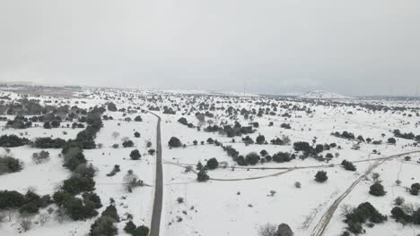 Descending-drone-aerial-view-of-snow-covered-countryside,-fields-and-road,-Israel