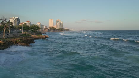 Aerial-flyover-wavy-coastline-of-Santo-Domingo-along-Avenida-George-Washington-during-golden-sunset