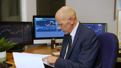 A-mature-business-man-reading-a-report-in-a-trading-office-at-his-desk