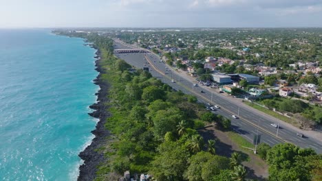 Aerial-flyover-LAS-AMERICAS-HIGHWAY-TOLL-STATION-along-coastline-with-traffic-on-Dominican-Republic