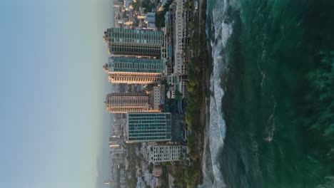 Vertikale-Luftaufnahme-Des-Welligen-Karibischen-Meeres-Und-Der-Avenida-George-Washington-In-Santo-Domingo-Mit-Skyline-Bei-Goldenem-Sonnenuntergang