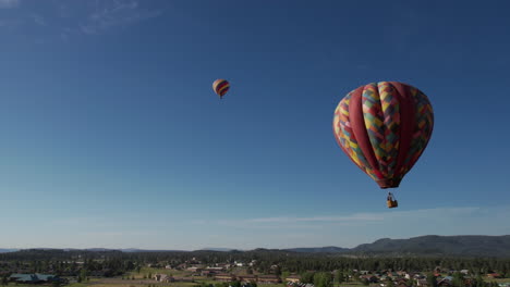 Drone-Shot-of-Hot-Air-Balloons-Flying-Under-Blue-Sky-and-Above-Green-Landscape