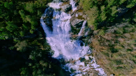 Aerial-top-down-shot-of-stunning-waterfalls-falling-down-into-river-surrounded-by-deep-forest-in-sunlight