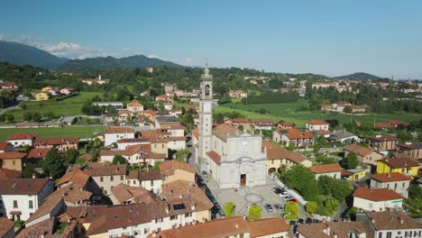 Aerial-drone-shot-over-a-cathedral-and-a-town-with-the-blue-sky-on-the-horizon-in-Pagnano,-Lombardy,-Italy