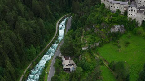 Aerial-View-Of-Torrente-Aurino-River-With-Pan-Up-To-Reveal-Taufers-Castle-In-Forested-Valley-Hills-Of-South-Tyrol