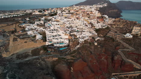 Drone-Shot-of-Santorini-Island-and-Oia-Village,-Greece,-White-Buildings-on-Top-Of-Red-Cliffs