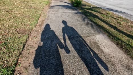 Unrecognizable-shadow-of-an-amorous-couple-holding-hands-as-they-walk,-projecting-onto-the-sidewalk