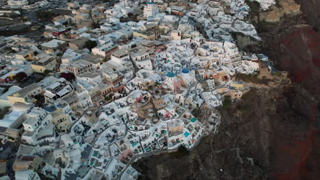 Vista-Aérea-De-La-Isla-De-Santorini-Grecia-En-El-Crepúsculo,-Casa-Blanca-Tradicional-En-Acantilados-Sobre-El-Mar,-Disparo-De-Drones