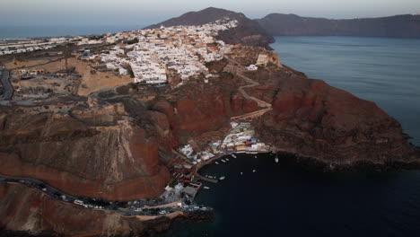 Aerial-View-of-Santorini-Island,-Greece,-Port-Under-Oia-Village-and-Red-Volcanic-Cliffs,-Drone-Shot