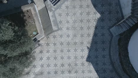 Top-down-aerial-backwards-panning-view-of-famous-chapel-of-Santo-Amaro-sidewalk-with-some-trees-shadows-in-Lisbon,-Portugal