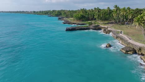 Aerial-flyover-coastline-of-La-Caleta-Boca-Chica-with-rocky-shore-and-palm-trees-during-sunny-day,-Dominican-Republic