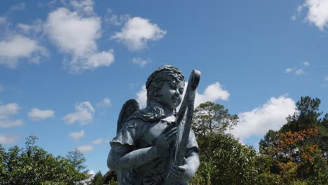 Escultura-De-Arcilla-De-Un-ángel-Con-Un-Arpa,-Sobre-Un-Fondo-De-Cielo-Azul