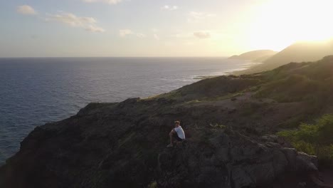 Mann-Ruht-Sich-Bei-Sonnenuntergang-Auf-Einem-Felsigen-Hügel-Aus-Und-Wandert-In-Makapuu,-Hawaii-–-Dolly-Pan-Aus-Der-Luft