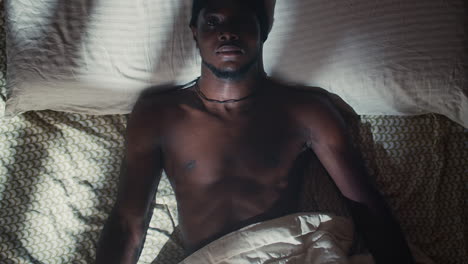 Young-black-bare-chested-man-with-open-eyes-in-bed,-overhead-pull-out