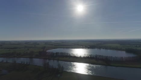 Beautiful-full-wide-drone-shot-of-flat-farm-fields-with-river-and-lake