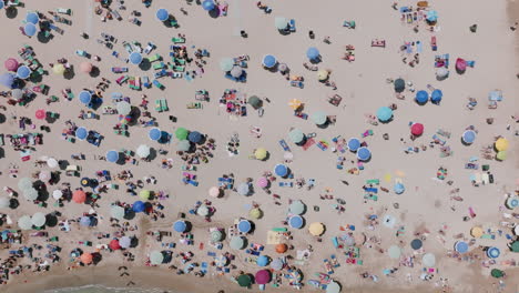 Top-down-aerial-footage-moving-away-from-tourists-on-the-beach-with-an-assortment-of-colors-in-Bari,-Italy