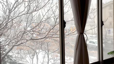 Living-at-home-in-cold-freezing-frozen-winter-when-snowfall-light-snow-cover-the-tree-and-street-people-walking-with-umbrella-car-driving-to-city-center-curtain-on-window-warm-house-scenic-landscape