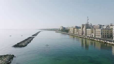 Wide-aerial-footage-of-the-Adriatic-Sea-in-front-of-the-city-of-Bari,-Italy-with-rowers-exercising-across-the-water