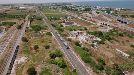 Static-aerial-footage-that-follows-a-passenger-train-in-Bari,-Italy-as-it-passes-underneath