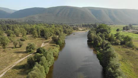 Drone-video-flying-over-Nestos-river-Greece-on-a-sunny-day-summer-,-trees-on-the-shore-bank-left-and-right-,-a-mountain-in-the-distance