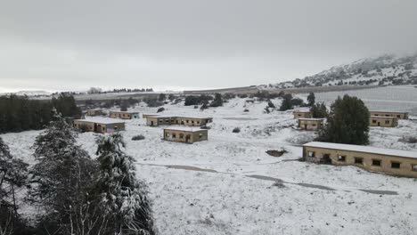 Abandoned-military-base-barracks-in-Israel-covered-in-snow,-drone-flyover,-low-level