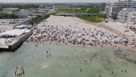 Aerial-footage-flying-towards-the-beach-from-the-green-Adriatic-Sea-showing-tourists-sunning-and-swimming-in-Bari,-Italy