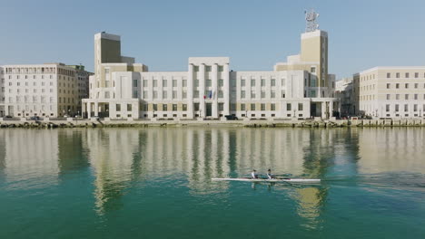 A-team-of-rowers-going-by-a-municipal-building-in-Bari,-Italy-in-the-early-morning