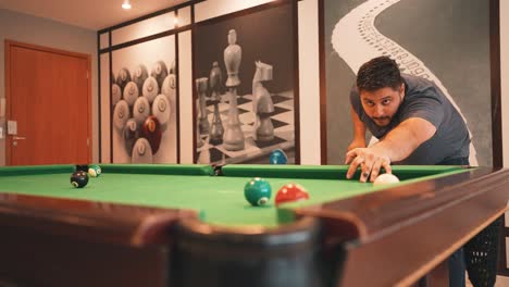 Young-man-sinking-brown-ball-number-seven-into-a-pocket-casual-sports-game-of-billiards-on-a-green-cloth