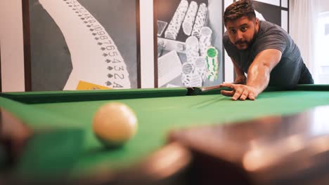 Young-bearded-man-sinking-red-ball-number-three-into-a-pocket-casual-sports-game-of-billiards-on-a-green-cloth