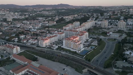 Aerial-footage-of-São-Pedro-do-Estoril-with-moving-trains,-Cascais,-Portugal-at-sunrise