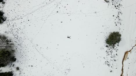 Man-laying-in-snow-making-snow-angel,-top-view,-zoom-out,-Israel,-Odem-Forest