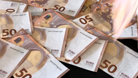 Viele-50-Euro-Banknoten-Fallen-Einer-Nach-Dem-Anderen-Auf-Einen-Dunklen-Tisch