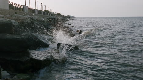 Slow-motion-aerial-footage-of-small-waves-crashing-against-the-rocks-in-Bari,-Italy-during-sunset
