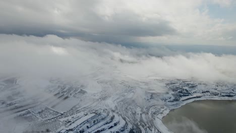 Pulling-back-aerial-view-of-Lake-Ram-covered-in-snow-with-dense-clouds,-Israel