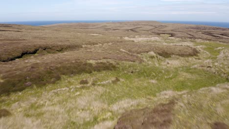 Drone-shot-of-a-peat-land,-containing-peat-banks-used-for-cutting-peat-for-fuel,-with-a-lighthouse-in-the-background