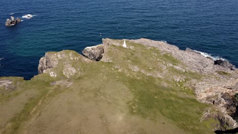 Tilting-drone-shot-of-a-lighthouse-surrounded-by-cliffs-and-nesting-sea-birds