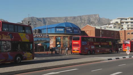 Double-decker-tour-buses-pull-up-outside-Cape-Town-Aquarium,-S-Africa