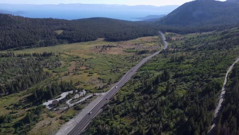 Toma-Aérea-Después-De-Un-Automóvil-Que-Conduce-Por-La-Carretera-Para-Revelar-El-Lago-Tahoe-Y-Las-Montañas-Circundantes