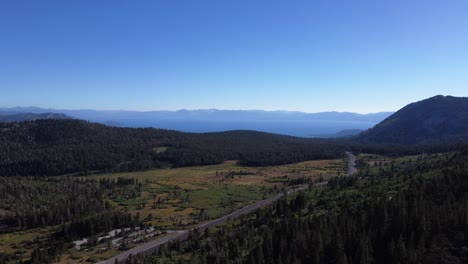 Toma-Aérea-De-Autos-Conduciendo-A-Través-De-Un-Impresionante-Valle-Salpicado-De-árboles-Hacia-El-Lago-Tahoe-En-Nevada