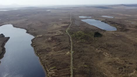 Drone-shot-of-a-single-track-road-through-a-moorland-and-peatland-landscape,-surrounded-by-lochs