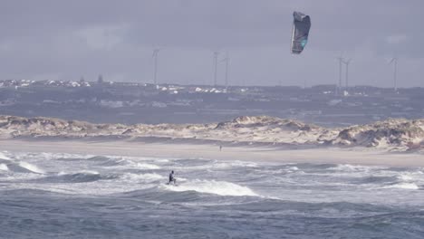 Kiteboarding-on-rough-sea-waves-of-Peniche,-Portugal,-windmills-and-city-in-background