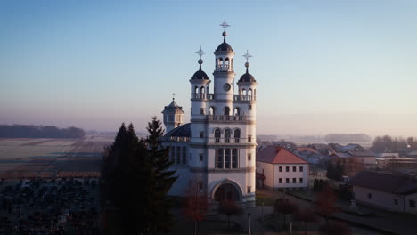 Drone-shot-of-a-big-church-in-a-small-village-on-flat-lands-in-early-morning-hours,-clear-sky-with-no-clouds