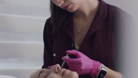 Woman-of-color-cosmetic-surgeon-nurse-injecting-botox-into-patient's-cheek,-slow-motion