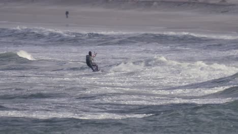 Kiteboarding-is-popular-water-sport-for-windy-weather,-kiteboarder-jumping-on-big-waves-in-Peniche,-Portugal