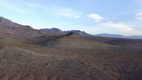 Luftaufnahme-Eines-Einzelnen,-Einsamen-Hügels,-Der-Sich-Durch-Die-Wüstenlandschaft-Erhebt,-Mit-Atemberaubenden-Bergen-Im-Hintergrund