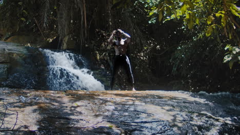Shirtless-Athletic-African-Man-Standing-on-a-Rock-by-the-Waterfall-in-Tropical-Forest-Looking-up---zoom-out,-low-angle